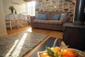 A cozy living room with a sofa, a table with chairs, a fireplace, and a rug. - Little Rogeston Cottage, Nolton Haven (Nolton Haven)