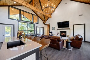 Un amplio salón con un gran ventanal, chimenea, sofá y televisor montado en la pared.