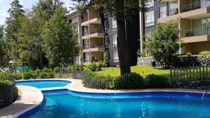Une piscine au design incurvé, entourée d’une clôture et de verdure.