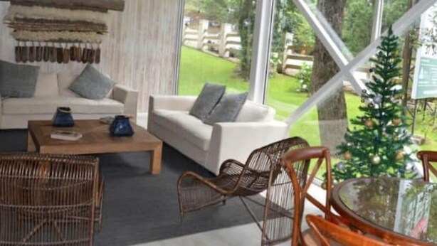 Un salon chaleureux avec un canapé, une table basse et des fauteuils en osier, donnant sur un jardin verdoyant et un sapin de Noël.