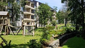 Un immeuble à plusieurs étages doté de balcons, entouré de verdure et bordé d’un chemin pavé de pierres.