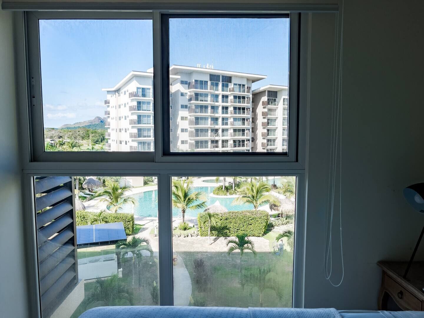 A hotel room with a large window overlooking a pool and a building with multiple balconies.