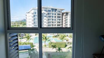 A hotel room with a large window overlooking a pool and a building with multiple balconies.