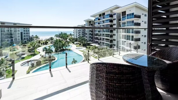A balcony with a view of a swimming pool, palm trees, and a beach. - Sea View Breeze -V3-4C- 2 bed, 2 bath (Punta Chame)