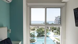 A room with a large window offering a view of a pool and resort area. - Sea View Breeze -V3-4C- 2 bed, 2 bath (Punta Chame)
