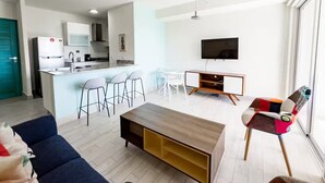 A modern living room with a sofa, a coffee table, a TV, and a kitchen area with bar stools. - Sea View Breeze -V3-4C- 2 bed, 2 bath (Punta Chame)