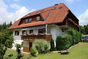 A two-story house with a sloped red-tiled roof, wooden balcony with flower boxes, and a well-maintained garden. - Apartment "Liebeslaube" with Shared Garden and Wi-Fi (Friedenweiler)