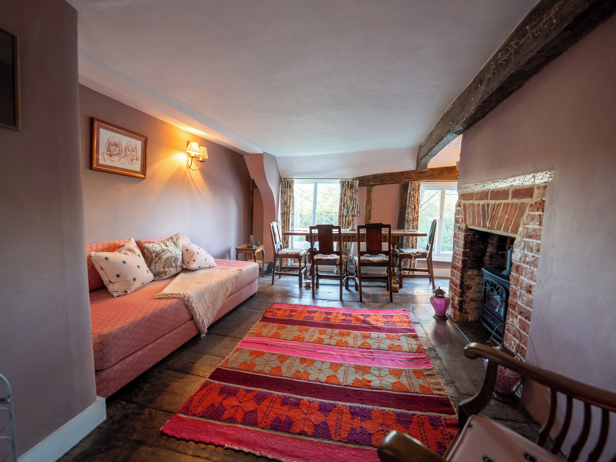 A cozy living room with a sofa, a patterned rug, a dining table with chairs, and a fireplace.