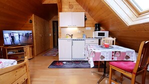 Una cabaña acogedora con interior de madera, una kitchenette, un comedor con mesa y sillas, y un televisor en la sala.