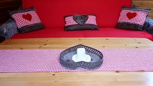 Un sofá rojo con almohadones con forma de corazón y una mesa de madera con mantel a cuadros.