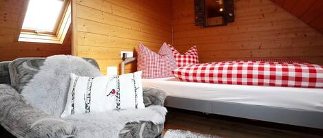 A cozy room with a bed, a chair, a window, and a wall-mounted clock.