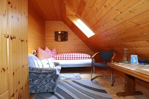 A cozy attic bedroom with a bed, a chair, a desk, and a skylight.