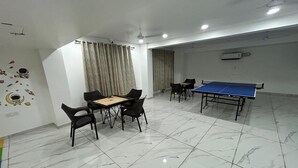 Une pièce avec une table de ping-pong, une petite table avec des chaises et un ventilateur au plafond.