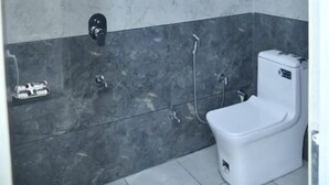A modern bathroom with a glass shower enclosure, a white toilet, and a marble-tiled wall. - HOTEL SHIVANSH (Sikar)