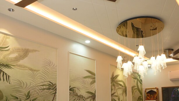 A modern hotel room with a ceiling fan, recessed lighting, a wooden bench, and tropical-themed wall art. - HOTEL SHIVANSH (Sikar)