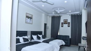 A modern hotel room with two beds, a sofa, a TV, and a ceiling fan. - HOTEL SHIVANSH (Sikar)