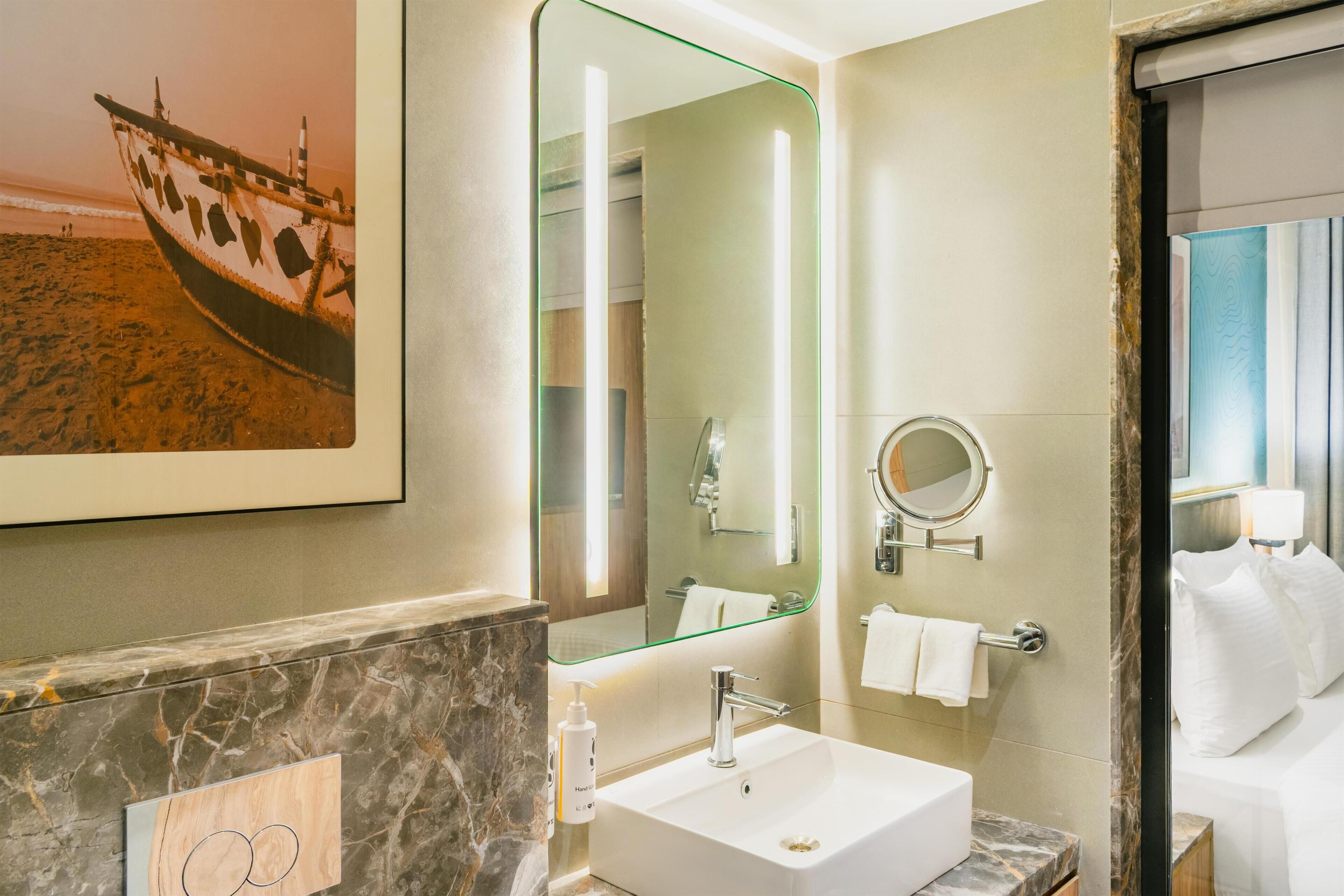 A modern bathroom with a marble sink, a large mirror, and a framed picture of a boat on the wall.