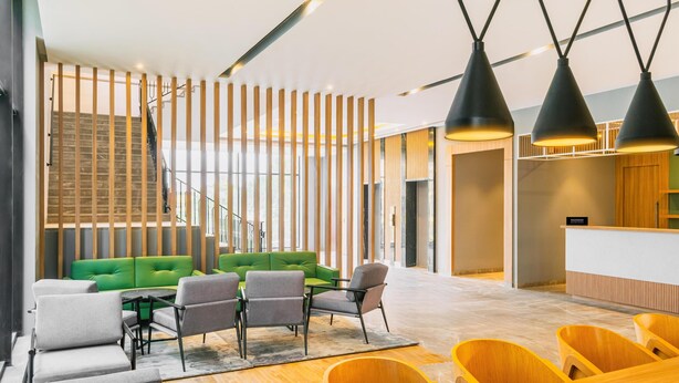 A modern interior with a staircase, green seating area, wooden reception desk, and pendant lighting. - Park Inn & Suites By Radisson, Puri (Puri)