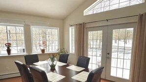 A dining room with a wooden table, six chairs, and large windows with curtains. - Huge home w/Game Room, Grill, Hot Tub, 3 living room, 2 bonus room, top location (Albrightsville)