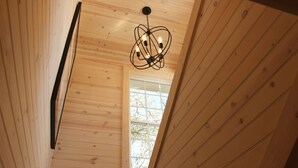 A wooden ceiling with a modern chandelier and a window with a view of trees.