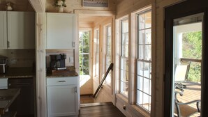 A wooden cabin interior with a kitchen area, a staircase, and large windows.