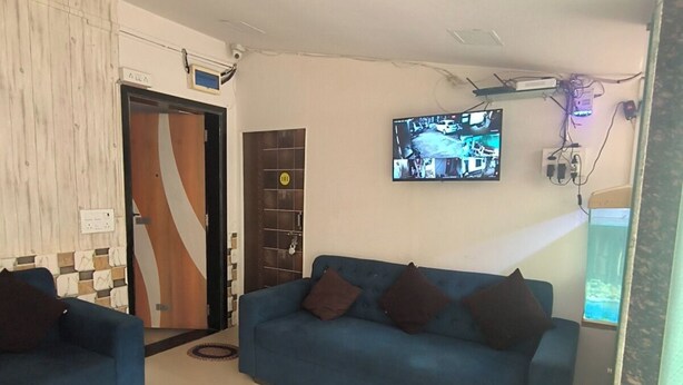 Un salón con dos sofás azules, un televisor montado en la pared y una puerta con cámara de seguridad.