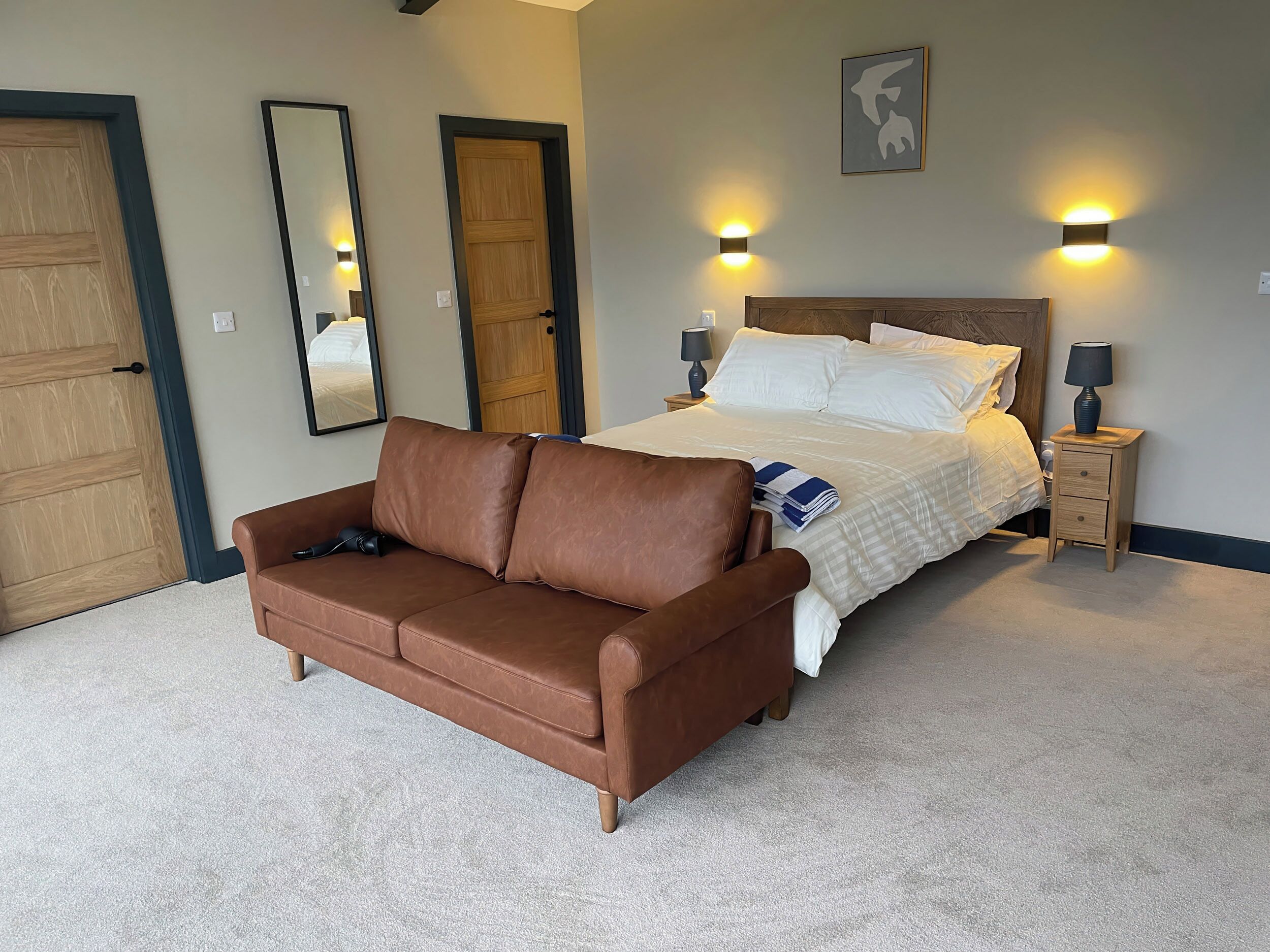 Une chambre à coucher avec un grand lit, deux lampes de chevet, un canapé en cuir marron et deux lampes fixées au mur.