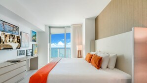 Ein modernes Hotelzimmer mit einem großen Bett, einem Schreibtisch mit einem Laptop und Blick aufs Meer durch die Glastür.