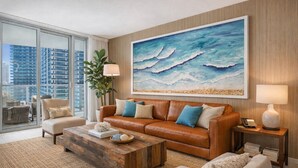 Ein modernes Wohnzimmer mit einem großen Gemälde zum Thema Meer, einer Ledersofa und Blick auf hohe Gebäude.