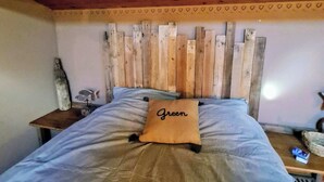 Een bed met een houten hoofdbord, een kussen met de tekst 'Green' en een nachtkastje met een lamp.