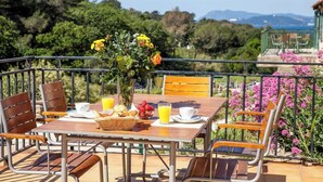 A wooden table set with breakfast items, a vase of flowers, and a scenic view of greenery and mountains. - Pinot - Domaine de la Navicelle (Le Pradet)
