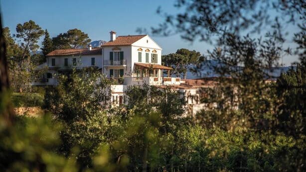 A large, white building with a red-tiled roof, surrounded by lush greenery and trees. - Pinot - Domaine de la Navicelle (Le Pradet)