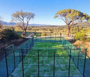 A view of a golf course with a green netted area and trees in the background.