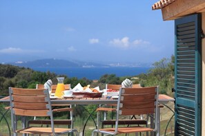 Una mesa al aire libre con sillas, una cesta de pan, una jarra de jugo de naranja y un bol de fresas.