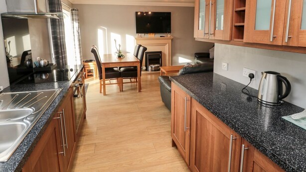 A modern kitchen with wooden cabinets, a granite countertop, and a built-in stove. - Megstone (Chathill)