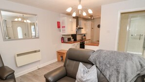 A modern living room with a leather sofa, a small wooden table, and a kitchen in the background. - Primrose Cottage (Chathill)