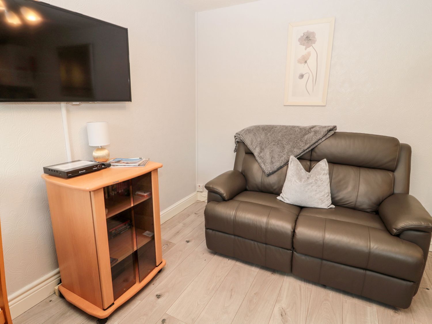 A living room with a brown leather sofa, a wooden TV stand, and a framed artwork on the wall.
