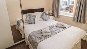 A neatly made bed with patterned pillows and a matching throw, a bedside table with a lamp, and a window with curtains. - Primrose Cottage (Chathill)