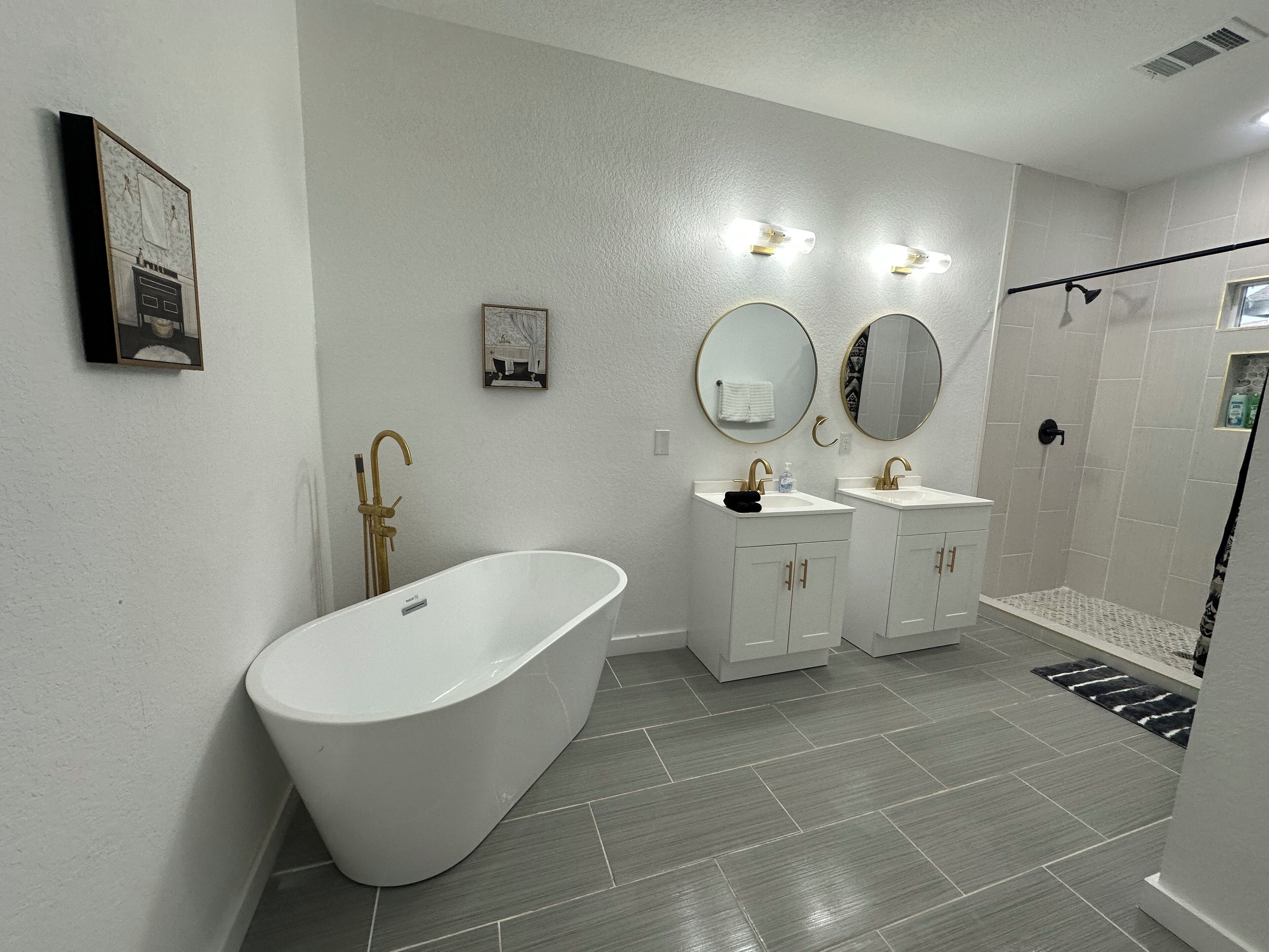 Een moderne badkamer met een vrijstaand bad, twee wastafels met gouden details en een inloopdouche.
