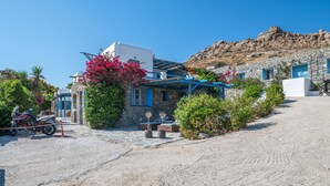 Un edificio de piedra con techo azul, una motocicleta estacionada en frente y un promontorio rocoso al fondo.