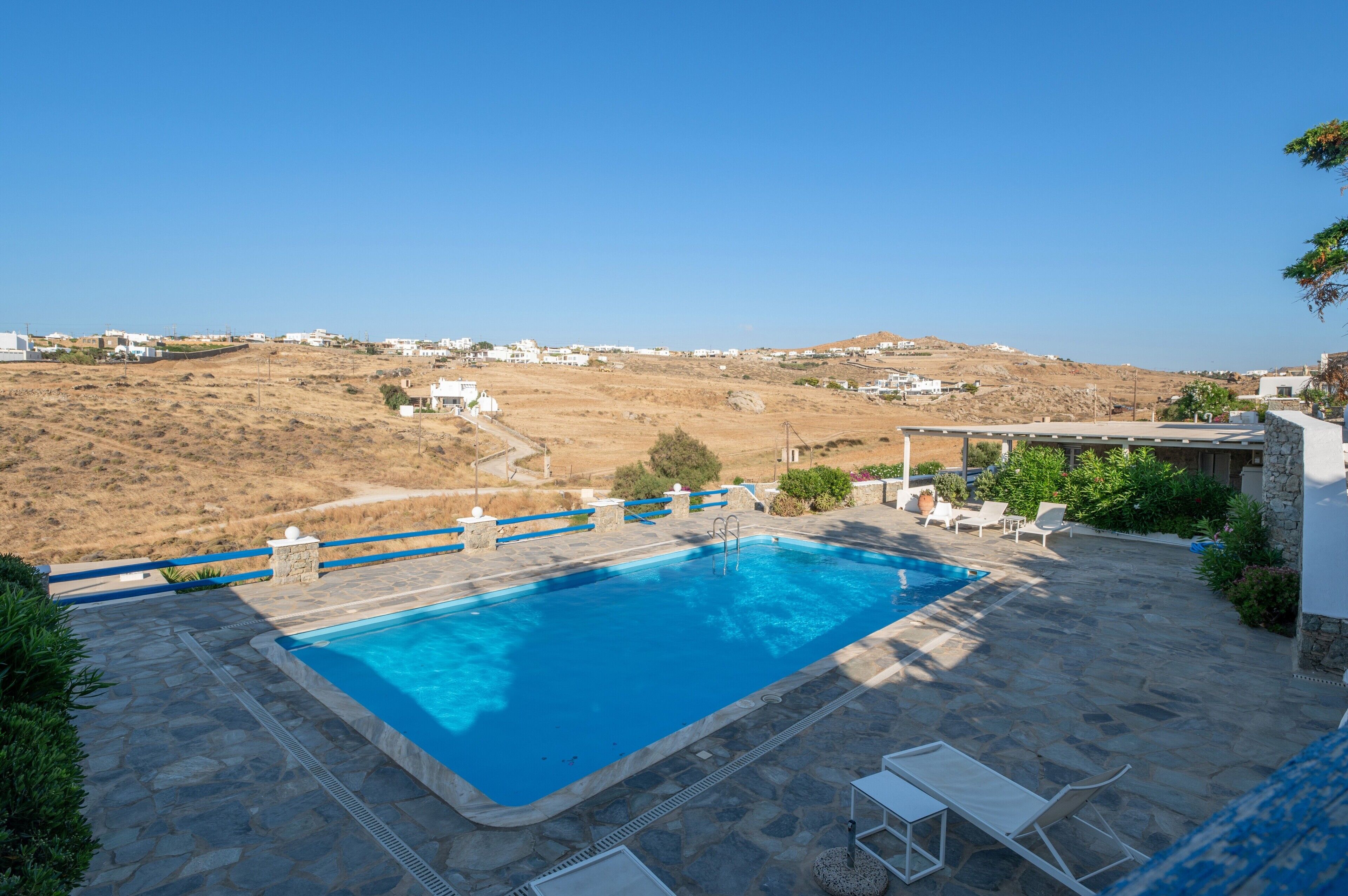 Piscina con terraza de piedra, sillas de descanso y vistas a un pueblo en la ladera.