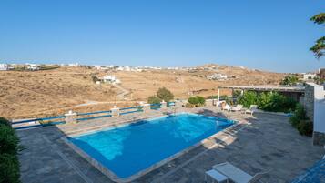 Piscina con terraza de piedra, sillas de descanso y vistas a un pueblo en la ladera.