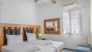 Hotellihuone, jossa on kaksi sänkyä, puinen pääty, peili, verhoilla varustettu ikkuna, tuoli ja ilmastointilaite.