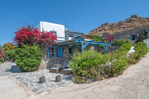 Un bâtiment en pierre avec une partie supérieure blanche, un auvent bleu et un chemin en pierre menant à un espace aménagé pour s’asseoir.