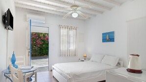 Quarto com cama, mesa de cabeceira, mesa com cadeira, ventoinha no teto e janela com cortinas.