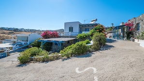 Un edificio costero con fachada de piedra, techo azul y un jardín con flores rosas.