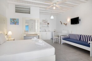 Une chambre d’hôtel équipée d’un lit, d’un canapé, d’un bureau, d’une chaise, d’une télévision et d’un ventilateur de plafond.