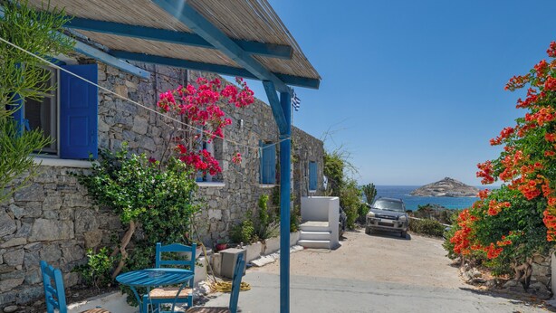 Un bâtiment en pierre avec une porte bleue, une table entourée de chaises et une voiture garée à l’arrière-plan.