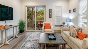 A living room with a sofa, coffee table, TV, and a sliding glass door leading to a patio. - Azure on 30A 1-205- A Wave From it All (Santa Rosa Beach)