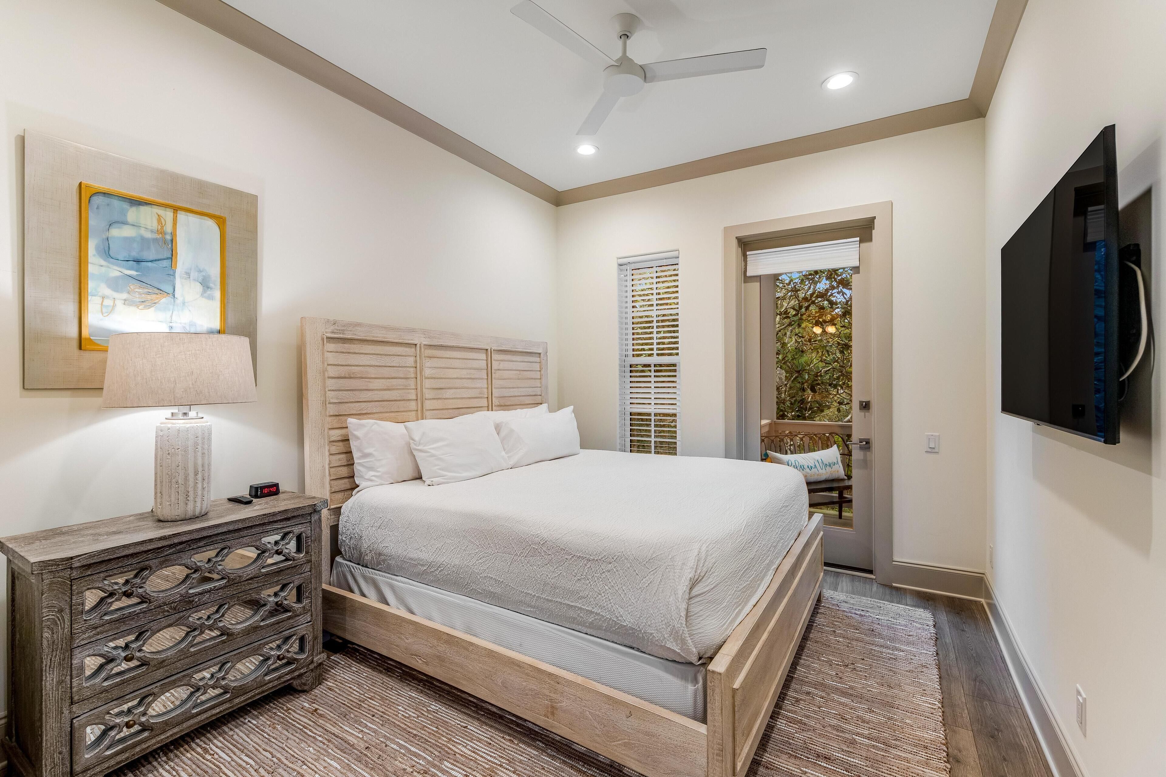 A bedroom with a bed, nightstand, lamp, artwork, and a TV mounted on the wall.
